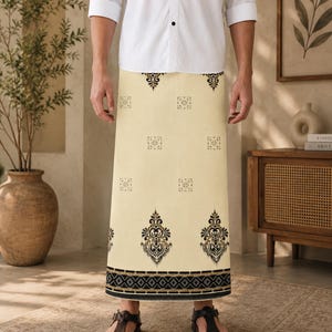 May include: A cream-colored sarong featuring a repeating black and gold damask-style pattern. The garment includes a wide, horizontal border at the hem with a detailed geometric design in black, gold, and white, worn with a white button-down shirt.
