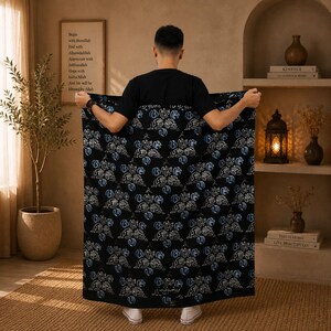 May include: A rectangular black textile featuring a repeating pattern of white and light blue calligraphic script. The fabric is held up to display the intricate, flowing lines of the text, which are arranged in a symmetrical, grid-like layout.