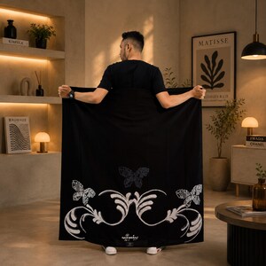 May include: A large rectangular black textile featuring a white embroidered design of three butterflies and scrolling floral patterns. The fabric is held horizontally, displaying the intricate white stitching against the solid black background.