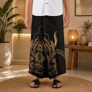 Könnte beinhalten: Ein schwarzer Sarong mit einem goldenen und braunen Phönix-Motiv und komplizierten Wirbelmustern. Der Stoff hat eine dezente Karostruktur und wird mit einem weißen Hemd getragen. Das Kleidungsstück fällt gerade bis zu den Knöcheln.