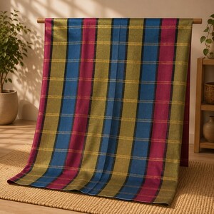 Puede incluir: Un tejido rectangular con un patrón de rayas verticales en tonos magenta intenso, azul vibrante y verde oliva. El diseño está acentuado por finas líneas horizontales de color oro metálico que se cruzan con los bloques de color.