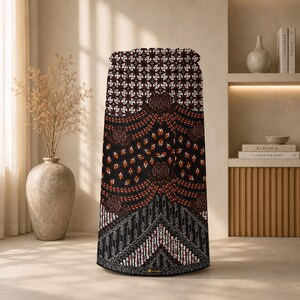 May include: A cylindrical fabric cover featuring a black base with intricate white, red, and brown geometric and floral patterns. The design includes repeating motifs, curved lines, and detailed borders, creating a structured visual texture.