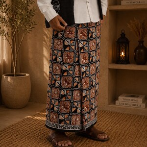 May include: A pair of wide-leg trousers featuring a repeating geometric pattern in shades of brown, black, white, and orange. The fabric displays a grid-like design with intricate floral and triangular motifs within each square, finished with a hem.