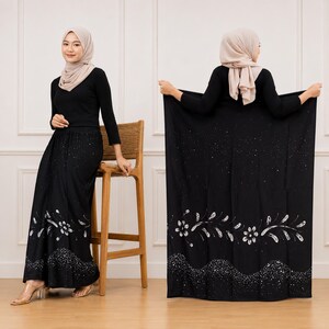 Può includere: Una maglia nera a maniche lunghe e una gonna nera abbinata con un motivo floreale bianco vicino all'orlo, arricchito da dettagli glitterati argentati. L'insieme è completato da un foulard beige, creando un outfit coerente e coordinato.