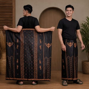 May include: A black sarong featuring a repeating copper-colored geometric diamond pattern and vertical borders with ornate floral motifs. The fabric is displayed fully extended and also wrapped around the waist, paired with a plain black t-shirt.
