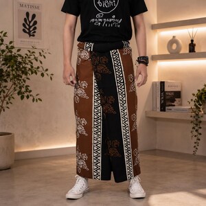 May include: A wrap-around skirt featuring a brown and black color palette with white geometric and organic patterns. The garment has a wide central black panel flanked by brown sections, all decorated with repeating white motifs and vertical borders.