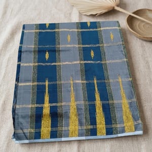 Könnte beinhalten: Ein gefaltetes Textil mit einem Gittermuster aus dunkelblauen und grauen rechteckigen Blöcken. Der Stoff ist mit dünnen, vertikalen und horizontalen goldenen Metallic-Linien sowie kleinen, sich wiederholenden goldenen Rautenmotiven verziert.