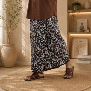 May include: Wide-leg trousers featuring a dark brown base with a repeating white and light blue floral and leaf pattern. The trousers are paired with a solid brown top and brown leather slide sandals, creating a coordinated ensemble.