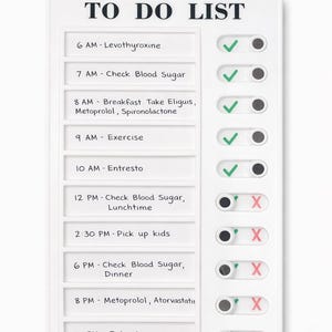 May include: A white plastic to-do list board with ten horizontal slots containing printed daily tasks and medication schedules. Each row features a sliding toggle switch on the right side, with green checkmarks for completed items and red X marks for incomplete tasks.