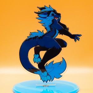 May include: A blue and black cartoon character figurine with a fluffy tail and ears, posed dynamically on a light blue circular base. The figurine is set against a warm orange background.