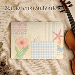 May include: A laptop hard shell case featuring a patchwork design of pastel blue and yellow stripes, gingham checks, and floral patterns. The case displays a pink hibiscus flower, a starfish, a butterfly, and the text POSTE GODWANA.