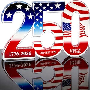 May include: A clear acrylic display piece shaped as the number 250, featuring a red, white, and blue American flag pattern. The text 1776-2026, 250 | EST.1776, and LAND OF THE FREE is printed on the front of the numerals in a bold, white font.