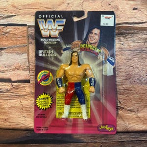 May include: A vintage action figure of the British Bulldog wrestler, packaged on a card. The figure is muscular, with red and blue wrestling attire. The packaging features the WWF logo and the wrestler's image.