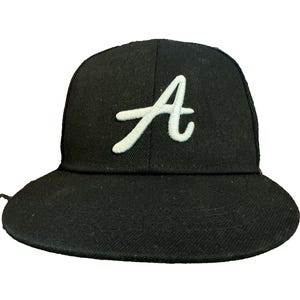以下が含まれることがあります： フロントパネルの中央に筆記体で刺繍された白い文字「A」が特徴の黒い野球帽。この帽子は構造化されたクラウンと平らなつばを備えており、全体が単色の黒い布地で構成されています。