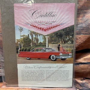 Puede incluir: Anuncio publicitario vintage de un coche Cadillac rojo. El anuncio presenta el logotipo de Cadillac y el texto "Where Craftsmanship is a Creed!". El coche está aparcado frente a un telón de fondo de árboles y un dosel rosa.
