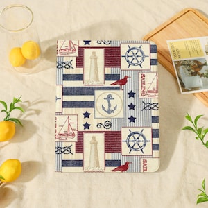 May include: A rectangular tablet case featuring a nautical pattern with navy blue stripes, red lighthouses, blue ship wheels, anchors, sailboats, and red birds. The design includes square frames and dark blue stars on a cream-colored background.