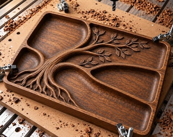 May include: A rectangular wooden serving tray featuring a carved tree design with roots and branches that create four distinct compartments. The dark brown wood grain is visible throughout the tray, which is secured by metal clamps on a workbench.
