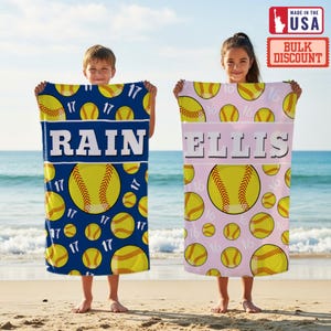 May include: Two personalized softball beach towels. One is navy blue with yellow softballs and the name "RAIN" in white. The other is light pink with yellow softballs and the name "ELLIS" in white. Both towels have the number 17 or 16.