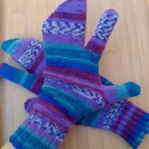 May include: Hand-knitted mittens in shades of purple, blue, and teal. The mittens have a striped pattern with a decorative design on the back of the hand and fingers. The cuffs have a scalloped edge.