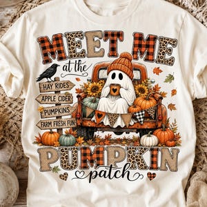 May include: A cream-colored t-shirt featuring a graphic of a ghost in a truck with the text MEET ME AT THE PUMPKIN PATCH. The design includes a wooden signpost with directions, pumpkins, sunflowers, a black crow, and autumn leaves in orange and brown.