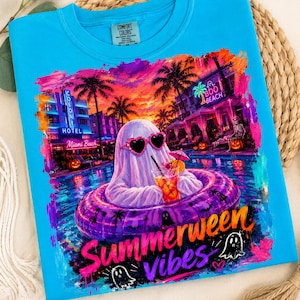 May include: A bright blue t-shirt featuring a graphic of a ghost wearing heart-shaped sunglasses in a purple pool float. The scene includes palm trees, a hotel, pumpkins, and the text "Summerween Vibes" in a stylized, colorful font.