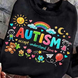 May include: Black sweatshirt with a colorful graphic design. The design includes the word "AUTISM" in rainbow colors, a smiling sun, a rainbow, hearts, stars, and the words "accept understand love". There are also drawings of a teddy bear, flowers, and children.