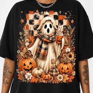 May include: A black t-shirt featuring a graphic of a ghost wearing a plaid scarf and holding a pumpkin-shaped cup. The design includes orange and black checkered patterns, autumn leaves, sunflowers, and several jack-o'-lantern pumpkins.