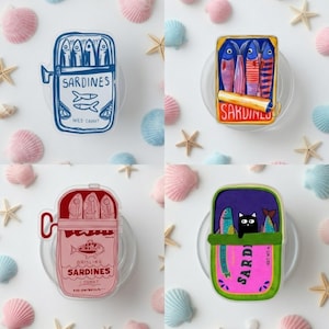 May include: Four whimsical sardine can designs. Each can features a different illustration of sardines, with text such as "Sardines" and "Wild Caught". The cans are set against a backdrop of seashells and starfish.