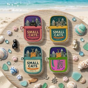 May include: Four rectangular tins labeled Small Cats in Seafood Jelly, each containing 112g. The tins feature illustrations of cats and fish in purple, yellow, teal, and pink. They are surrounded by small cat paw charms and seashells.