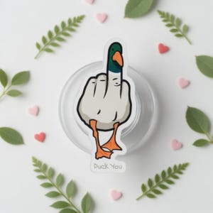 May include: A white sticker featuring a cartoon duck giving the middle finger. The duck has a green head, orange beak and feet, and the text "Duck You" is at the bottom. The sticker is on a clear, round surface.