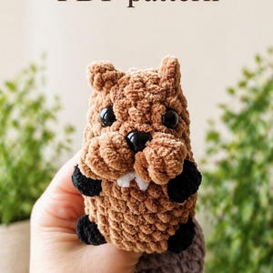 May include: A brown crocheted beaver plush toy with black plastic eyes, a black nose, and two small white teeth. The beaver has black paws and a textured brown body. The text "PDF pattern" is printed in brown above the plush toy.