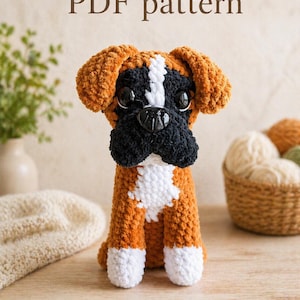 May include: A handmade crochet Boxer dog with brown, black, and white details. The dog has large black eyes and a black nose. The text "PDF pattern" is above the dog. The dog is sitting on a wooden surface.