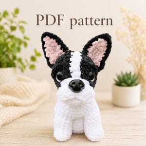 Puede incluir: Un perro Boston Terrier tejido a ganchillo con detalles en negro, blanco y rosa. El perro tiene orejas grandes y erguidas y una nariz negra. El texto "PDF pattern" se muestra encima del perro.