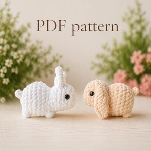 May include: Two crocheted bunny toys, one white and one beige, sit side-by-side. The white bunny has upright ears, while the beige bunny has floppy ears. Both have black safety eyes. The text "PDF pattern" is above the bunnies.