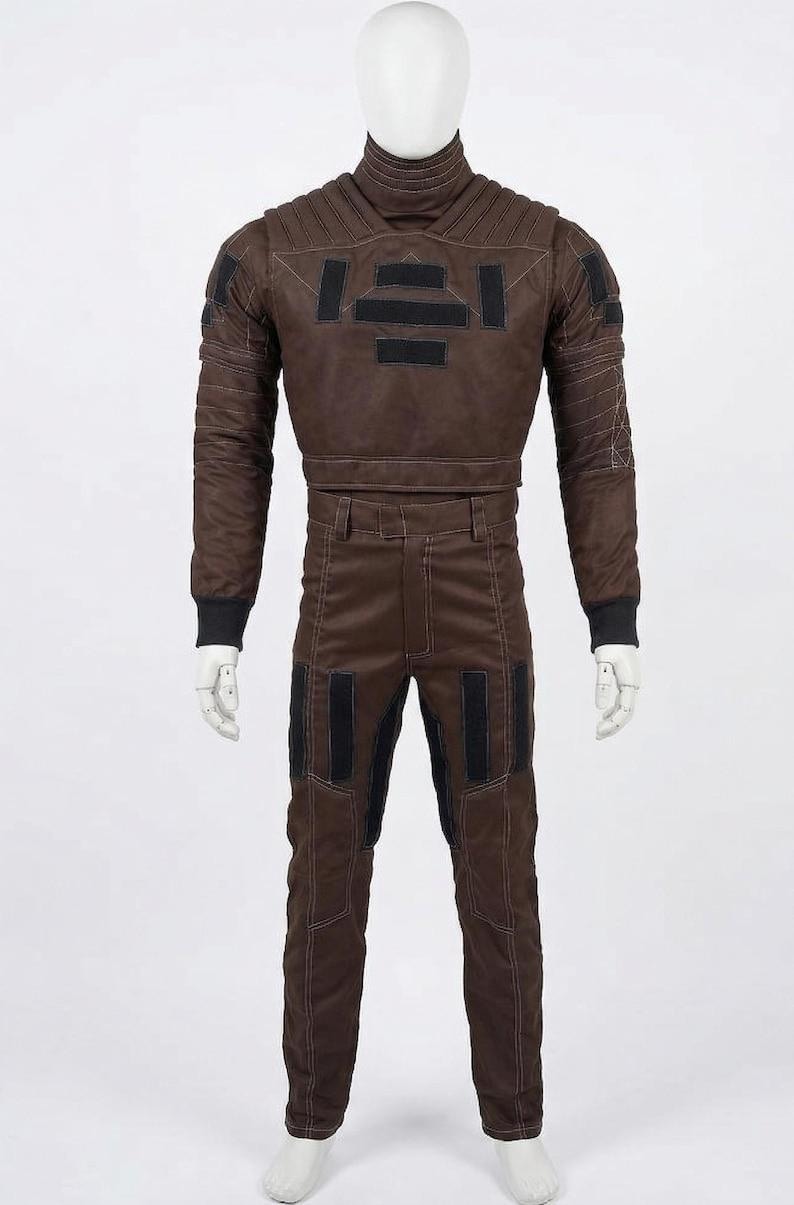 May include: Brown two-piece costume with black accents. The jacket has a high collar and rectangular patches. The pants have black knee patches. The costume is displayed on a mannequin. The outfit is likely for cosplay or a theatrical production.