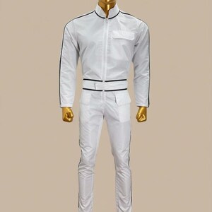 K&ouml;nnte beinhalten: Wei&szlig;er Overall mit schwarzen Zierleisten, Stehkragen und Rei&szlig;verschluss. Das Outfit umfasst eine Brusttasche, zwei H&uuml;fttaschen und ein G&uuml;rteldetail. Die Hose hat schwarze Streifen an den Seiten. Die Schaufensterpuppe ist goldfarben.