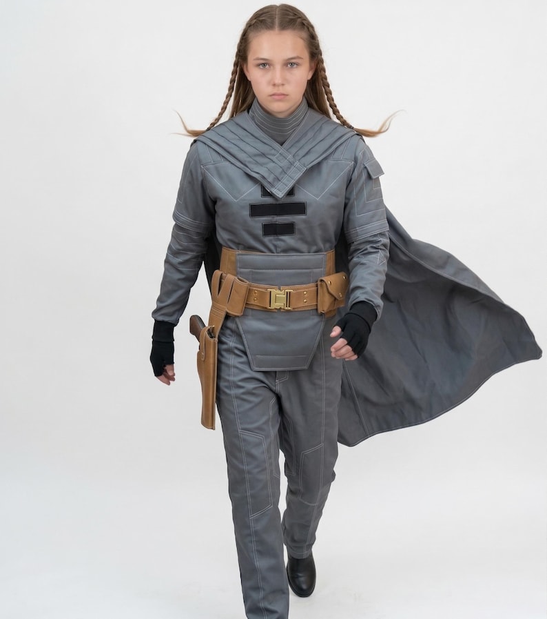 May include: A gray cosplay costume with a cape, belt, and holster. The outfit includes a high-collared top, pants, and a brown belt with a gold buckle. The costume is worn with black gloves and boots.