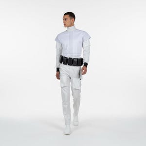 Puede incluir: Un atuendo blanco que consta de un cuello alto, una chaqueta corta, una camisa de manga larga y pantalones. El atuendo incluye un cintur&oacute;n negro con bolsillos y botas blancas. El modelo est&aacute; de pie frente a un fondo blanco.