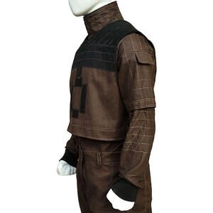 May include: Brown jacket with black accents and geometric stitching. The jacket features a high collar, a black panel across the shoulders, and a cropped design. The sleeves have a unique geometric pattern near the elbows, and the cuffs are black.