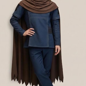 May include: A dark blue outfit with a brown cape. The outfit includes a long-sleeved jacket and matching pants. The cape has a jagged edge. The outfit is worn by a person with long, wavy brown hair.