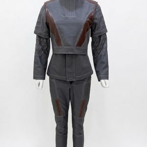 May include: A gray and brown futuristic-style outfit on a mannequin. The jacket has a high collar and brown accents on the shoulders and chest. The pants are gray with brown patches on the knees. White stitching details the seams.