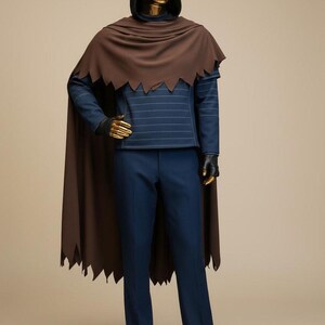 May include: A mannequin dressed in a dark brown cape with a jagged edge, a hooded black top, and navy blue pants. The top has horizontal white stripes. The mannequin's hands and face are gold.