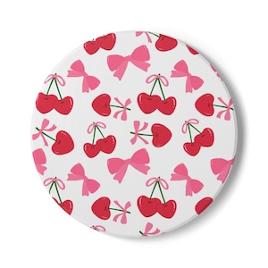 May include: A circular white coaster with a repeating pattern of red cherries and pink bows. The cherries have green stems, and the bows are tied with ribbons. This coaster is ideal for adding a touch of whimsy to any space.
