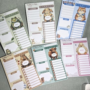 May include: Five rectangular daily planner notepads featuring animal illustrations including a frog, rabbit, cat, capybara, highland cow, and duck. Each notepad has the text Today's Plan, sections for Important, Goals, Notes, and Quote of the Day.