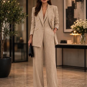 May include: A beige pinstripe suit featuring a double-breasted blazer with gold buttons and wide-leg trousers. The outfit is accessorized with sunglasses and a black clutch. This suit is a smart choice for business or formal events.