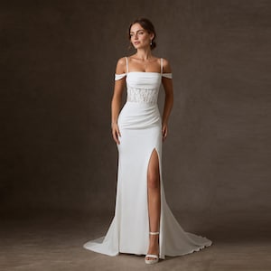 Puede incluir: Un vestido blanco hasta el suelo con un corpiño sin tirantes con finos tirantes, detalle de mangas caídas, una sección central de encaje transparente y una abertura lateral alta que se extiende desde el muslo hasta el dobladillo.
