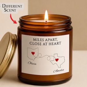 May include: A brown glass candle jar with a gold lid and a lit wick. The white label features the text "MILES APART, CLOSE AT HEART" above outlines of Ohio and Texas connected by a dashed line with red hearts, plus the names "Olivia" and "Amelia".