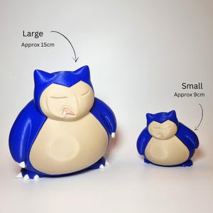 May include: Two blue and beige Snorlax figures with closed eyes and small white claws. The larger figure is labeled Large Approx 15cm and the smaller figure is labeled Small Approx 9cm. Both figures have a smooth, rounded body shape and a distinct facial expression.
