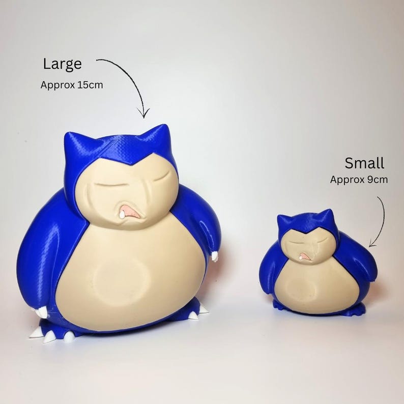 May include: Two blue and beige Snorlax figures with closed eyes and small white claws. The larger figure is labeled Large Approx 15cm and the smaller figure is labeled Small Approx 9cm. Both figures have a smooth, rounded body shape and a distinct facial expression.