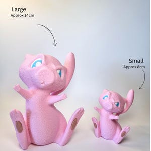 May include: Two pink textured figurines of a cat-like creature with blue eyes. The large figurine is labeled 'Large Approx 14cm' and the small figurine is labeled 'Small Approx 8cm'. Both figures are in a seated position with tails curved upward.